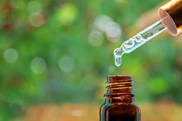 pipette with essence drop and bottle, closeup on blurred nature background. herbal essential massage oil dripping into bottle. spa beauty concept. selective focus - drop herbal medicine leaf perfume imagens e fotografias de stock