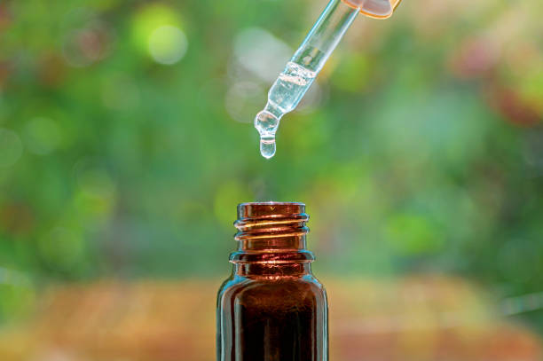 spa beauty concept. herbal essential massage oil dripping into bottle. pipette with essence drop and bottle, closeup on blurred nature background. selective focus - drop herbal medicine leaf perfume imagens e fotografias de stock