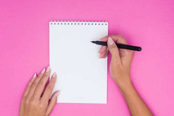istock Notebook with pen holds female hands on a pink background. 1184933992
