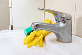 Sponge and gloves for washing dirty faucet with limescale, calcified water tap with lime scale on washbowl in bathroom, house cleaning concept