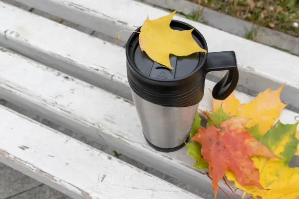 Season, autumn hot drinks and picnic concept - metal thermo coffee cup surrounded by colorful yellow leaves.