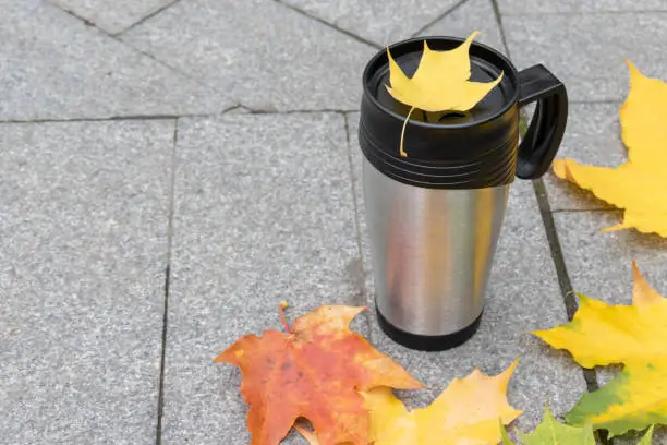 Season, autumn hot drinks and picnic concept - metal thermo coffee cup surrounded by colorful yellow leaves with copy space.