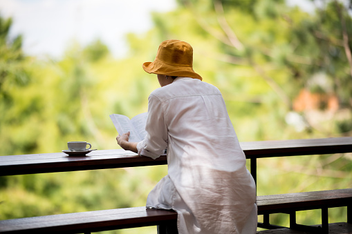 Middle aged woman sitting on the bench and reading a book in the park