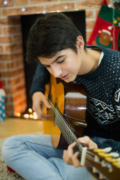 그의 기타를 연주하고 크리스마스 트리 근처 실내 노래하는 젊은 남자의 초상화 - suit jeans men musician 뉴스 사진 이미지