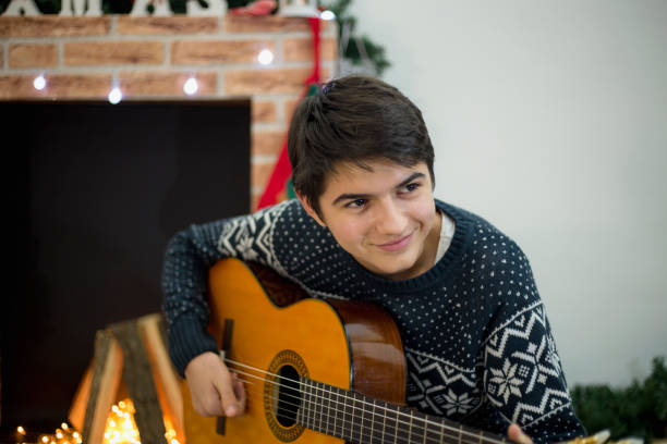 retrato de joven tocando su guitarra y cantando en el interior cerca del árbol de navidad - suit jeans men musician fotografías e imágenes de stock