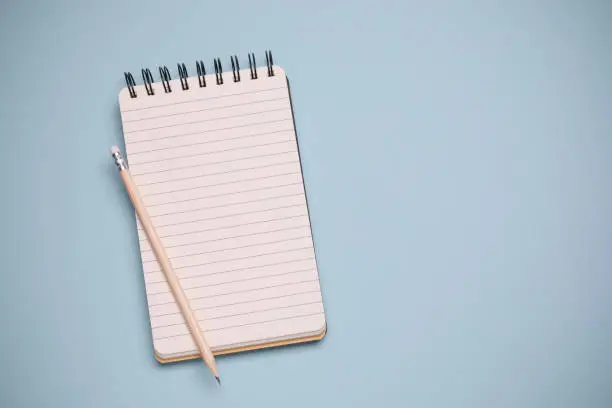 Spiral notebook and pencil on blue background