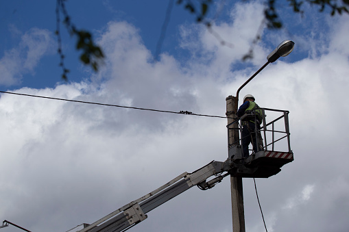 An electrician on a special lifting platform repairs a street lamp on a concrete pillar