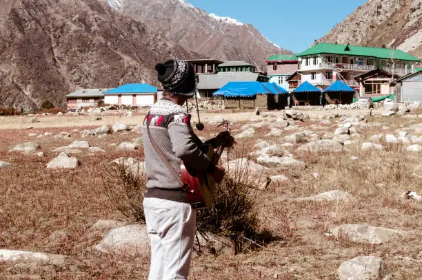 A solo traveler of Indian ethnicity and hobbyist  musician playing music with guitar on mountain valley. Alone in the silence of Himalayan mountain and sound of guitar strings. Summer music Inspiring environment in outdoors. Sangla Valley, Himachal Pradesh, India, South Asia.