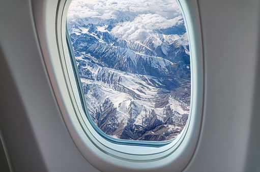 Incredible view from an airplane window on a snowy mountain range through the clouds. Flight over Georgia