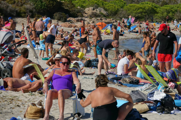 Masses of tourists sunbathe on sandy beach of famous island in the Mediterranean CORSICA, FRANCE - SEPTEMBER 2017: Masses of tourists sunbathe on a sandy beach of a famous island in the Mediterranean. Countless people on vacation flock to popular shore in Corsica on a sunny day. sea population stock pictures, royalty-free photos & images