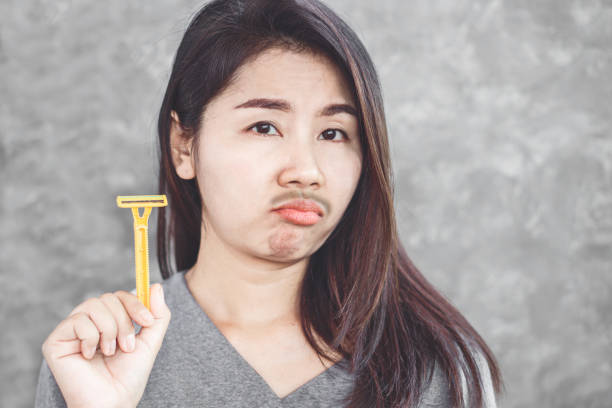 unhappy Asian woman having problem with mustache growing on face ,hand holding razor