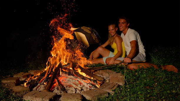 istock CLOSE UP: Handsome man strikes the fire with a branch while cuddling with woman. 1185001136