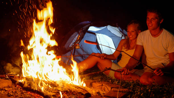 istock CLOSE UP: Smiling man strikes the fire with a branch while roasting frankfurters 1185002094