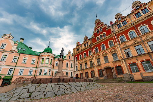 Old town hall of Vyborg city in Russia. Monument in foreground and blue cloudy sky in background.