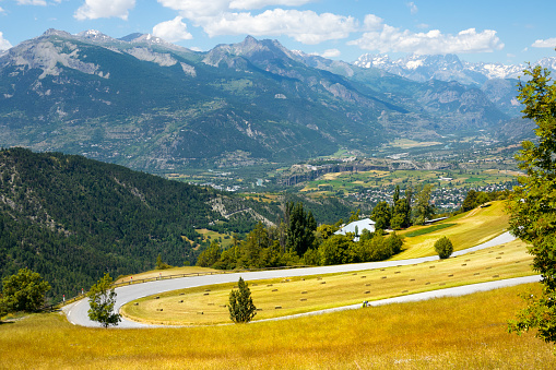 Empty mountain switchback road runs past the beautiful yellow meadows in the French Alps. Picturesque colorful landscape surrounds the famous road trip route running through the idyllic countryside.