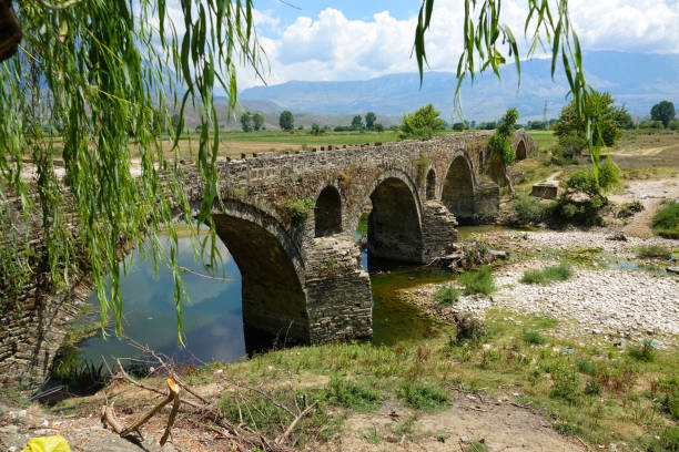 AERIAL Empty ottoman bridge in rural landscape crosses the drying up river. Flying over the stone bridge slowly decaying in the remote countryside in Albania. Heat and time breaking down arched bridge