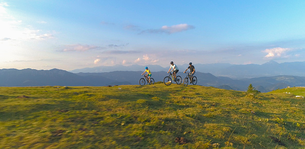 DRONE: Group of friends cross country cycling pedalling their bicycles uphill before speeding across the scenic meadow in the picturesque green Slovenian mountains. Extreme tourists mountain biking.