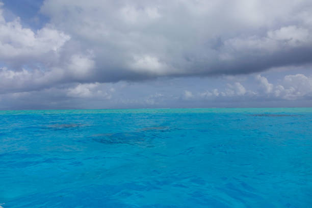 DRONE: Flying over the tranquil turquoise colored ocean on a cloudy summer afternoon. Spectacular view of the endless Pacific stretching out into the horizon and under the dark grey stormy clouds.