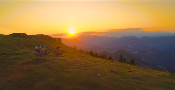 istock AERIAL: Three mountain bikers speeding down a grassy hill at golden sunset. 1185005927