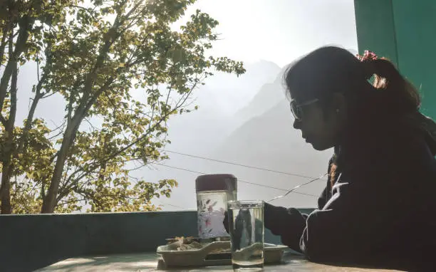 Woman having food taking breakfast while sitting on a dining table in morning at holiday home against Himalayas mountains background.