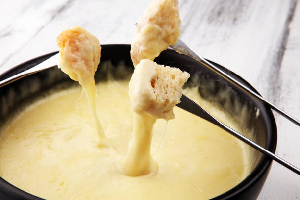 istock Gourmet Swiss fondue dinner on a winter evening with assorted cheeses on a board alongside a heated pot of cheese fondue with two forks dipping 1185007049