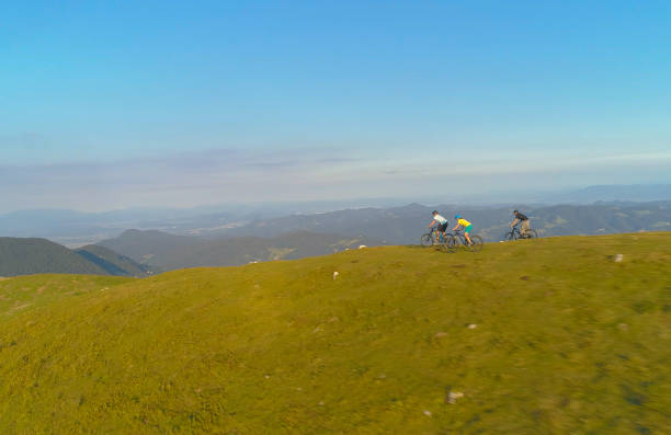 istock DRONE: Flying along three friends speeding down a grassy hill on mountain bikes. 1185008111