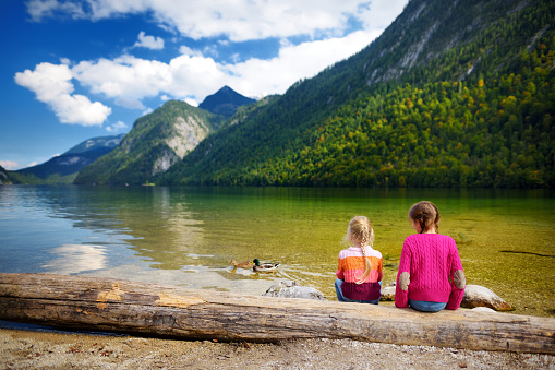 Two cute sisters enjoying the view of deep green waters of Konigssee, known as Germany's deepest and cleanest lake, located in the extreme southeast Berchtesgadener Land, Bavaria, Germany