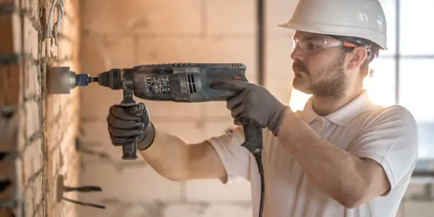 Handyman uses jackhammer, for installation, professional worker on the construction site. The concept of electrician and handyman. House and house reconstruction.