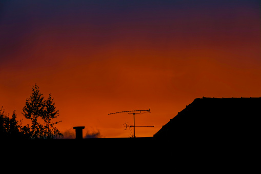 SILHOUETTE: Evening sky creates a contrast with a black silhouette of the roof of a house in the tranquil suburban neighborhood. Tv antenna sticks out into morning sky at picturesque summer sunrise.