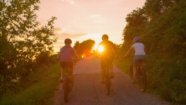 istock LENS FLARE: Unrecognizable cyclists pedal along the empty road at golden sunset. 1185019916