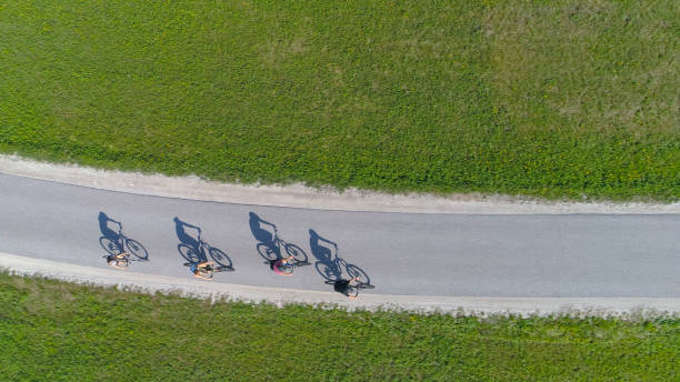 TOP DOWN: Four friends riding bikes casting shadows on the empty asphalt road.