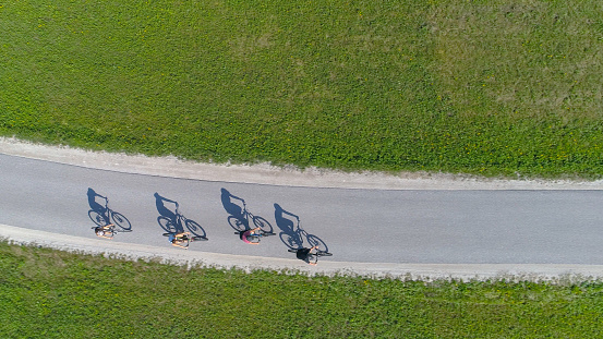 TOP DOWN: Four friends riding bikes casting shadows on the empty asphalt road while exploring the scenic sights of beautiful Slovenian countryside in the summer. Active tourists on a fun bicycle ride.