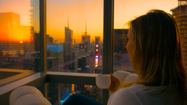 istock CLOSE UP: Woman observes the golden lit evening cityscape while drinking tea. 1185021170