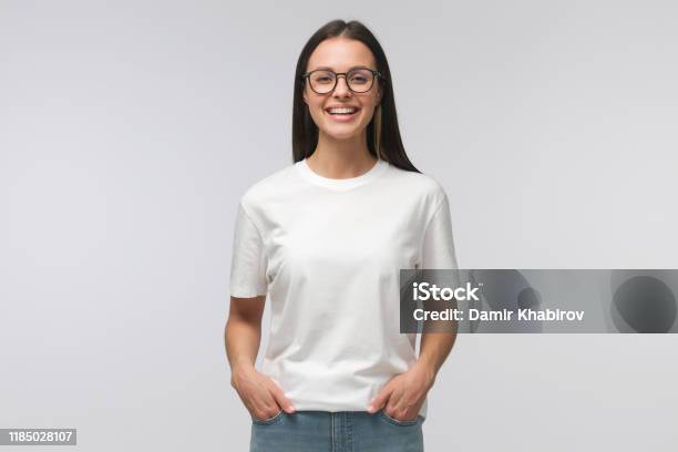 Young Laughing Woman Standing With Hands In Pockets Wearing Blank White Tshirt With Copy Space Isolated On Gray Background Stock Photo - Download Image Now