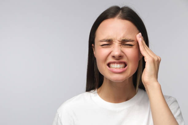 Headache concept. Young woman showing how much her head hurts, experiencing pain, looking miserable and exhausted, isolated on gray background Headache concept. Young woman showing how much her head hurts, experiencing pain, looking miserable and exhausted, isolated on gray background clenching teeth stock pictures, royalty-free photos & images