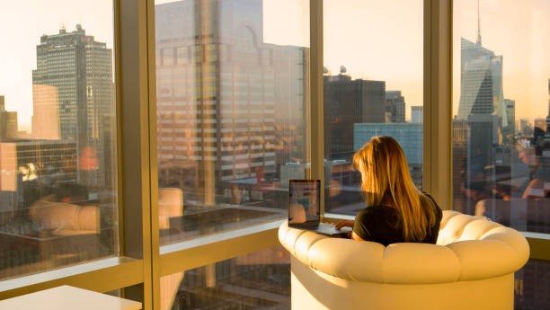 COPY SPACE: Woman working on her computer from her home office facing the city.