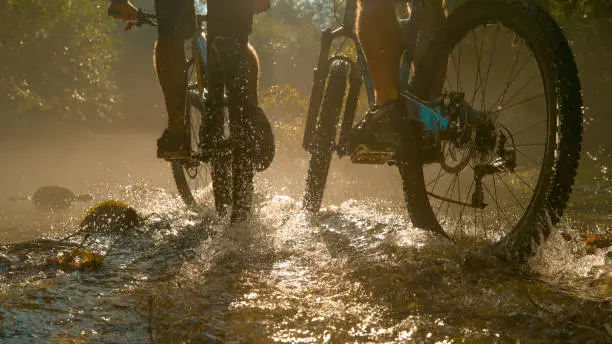 Photo of LOW ANGLE: Two unrecognizable persons riding new mountain bikes across stream.