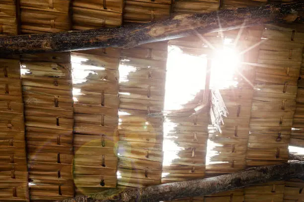 Close up of grunge palm thatch pieces in a row with sun ray  and flare shining through.
Thatched roof ,low angle view.