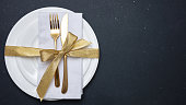 Gold cutlery on white set of dishes, black background, top view