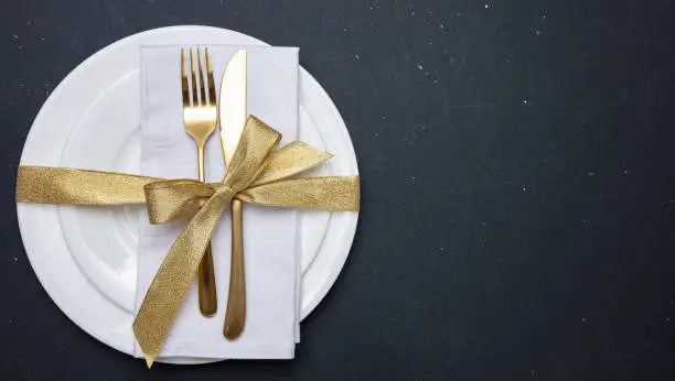 Table setting, luxury, formal. Gold cutlery on white set of dishes, black background, top view