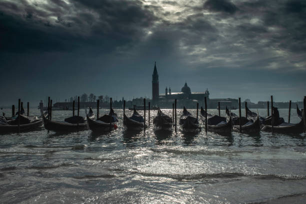 Gondolas, Venice, Italy Gondolas in front of St Mark's Square, with a view across to San Giorgio Maggiore just at the moment the storm light opens up and silver shows through. The waterfront is flooded. Taken during the acqua alta (high tide) that floods Venice each autumn and is getting worse. gondola traditional boat photos stock pictures, royalty-free photos & images