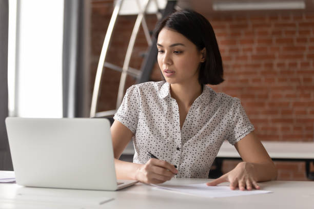 istock Focused asian business woman working looking at laptop making notes 1185049564