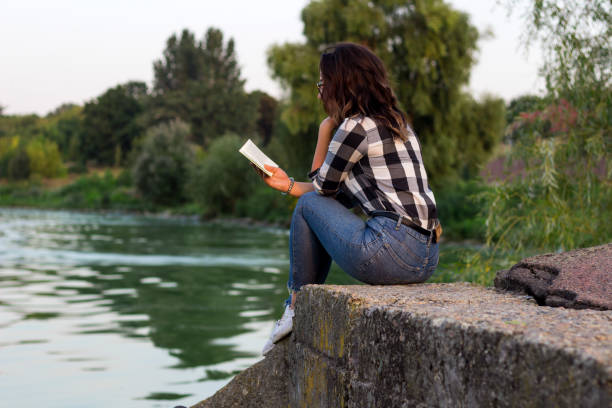 istock girl reading a notebook by the river on a concrete pier 1185052591