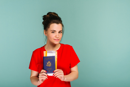 It's time to travel. A modern trendy smiling woman in red dress with air tickets and a passport in her hand.