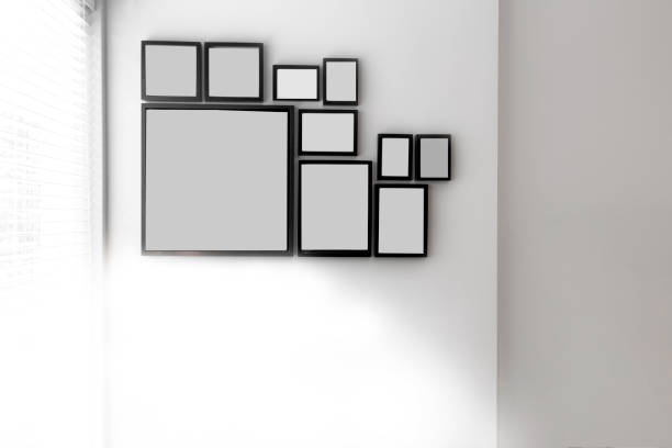 istock Group of various blank black picture frames on grey wall near a window with light, space for text 1185059754