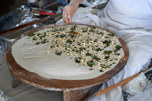 A woman cook, in the traditional manual way, bakes a Turkish gozleme cake in an old oven. Preparation of dough, kneading, rolling. The formation of the filling of cottage cheese, spinach. Baking cakes and dividing into portions