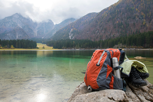 Orange backpack, black hiking boots and green anorak lying on a rock at the Lacs de Fusine in the Apls, Italy. Nikon D850.