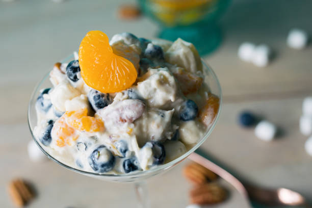 Clementine ambrosia in a martini glass. Made with blueberries, pineapple, coconut, marshmallows and pecans. Serving of clementine ambrosia in a martini glass, spilled marshmallows and pecans in the background. Close view ragweed stock pictures, royalty-free photos & images