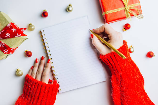 istock Gift expense planning, goals plans dreams. New Year and Christmas, concept writing in notebook. Female hands, red knitted sweater, gift box, Christmas balls on white background. Flat lay. Top view 1185079960
