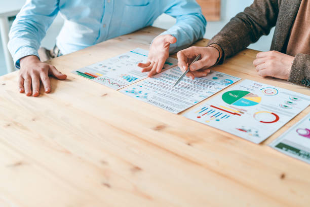 istock Two young businessmen sitting by wooden table while discussing documents 1185081088